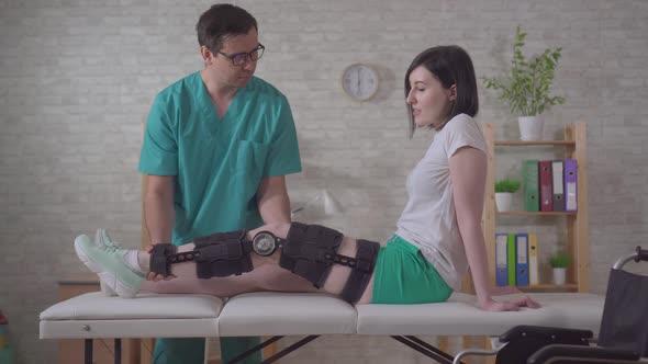 Male Physiotherapist Helps Dons Helps with Orthosis Knee Brace After Injury alt