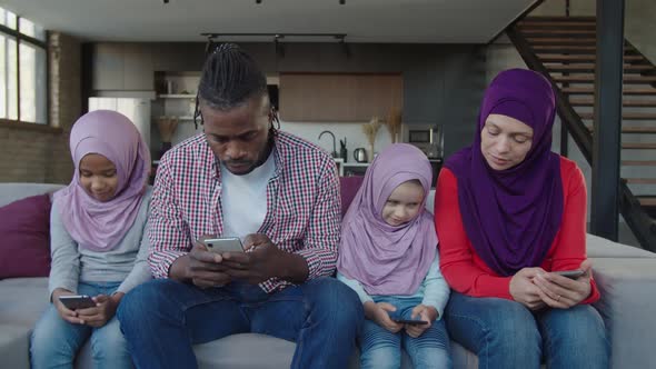 Positive Diverse Multiracial Muslim Family with Little Girls Browsing Online on Smartphones Indoor alt