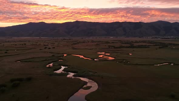 Flying backwards over river winding through the landscape at dawn alt