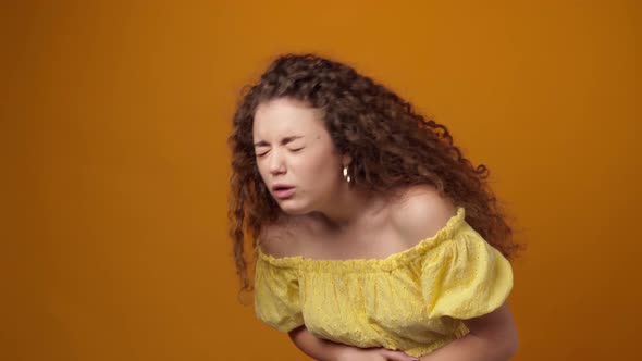 Young Woman Suffering Stomach Ache Against Yellow Background in Studio