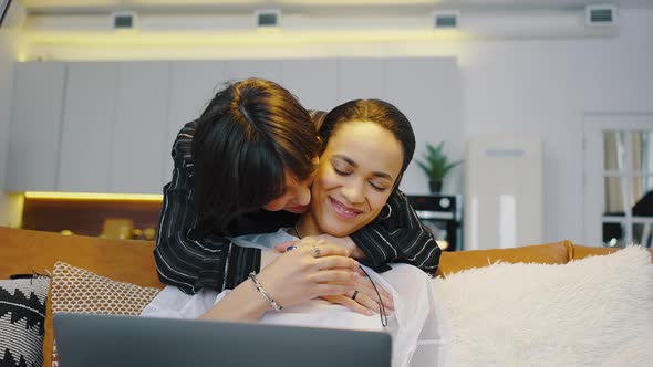 Two Lesbians at Home Girl Works Remotely with a Laptop While Sitting on the Couch Partner Comes alt