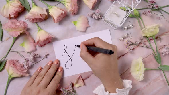 Hands writing SPRING on a card near pink flowers close up on a marble table alt