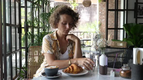 Caucasian Woman Takes Off Her Face Mask to Have a Coffee with Croissant in Stylish Cafe alt