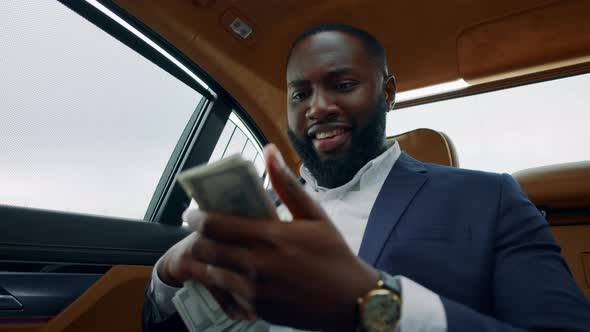 Closeup African Man Smelling Dollars at Car. Man Sitting with Money at Vehicle alt