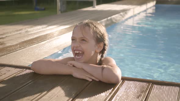 Cute Funny Girl with Pigtails Laughing, Showing Thumb Up Looking Out of the Pool alt