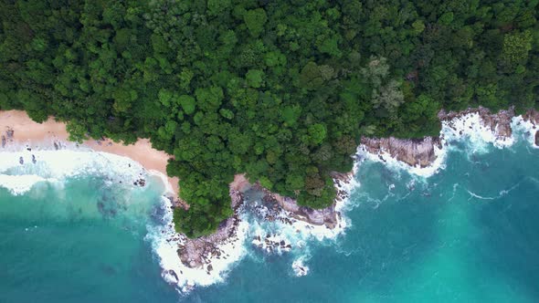 Aerial view of the tropical sea with wave crashing against an empty stone rocks cliff alt
