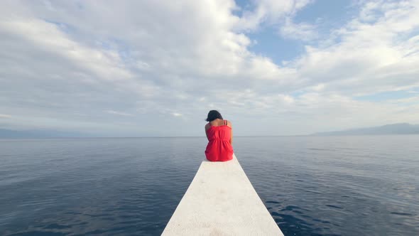 Back View of a Sad Young Woman Sitting Alone on the Edge of the Boat alt