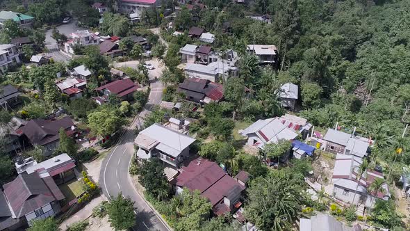 Indian village with road snaking through, surrounded by lush vegetation of tropical forest, drone fo alt