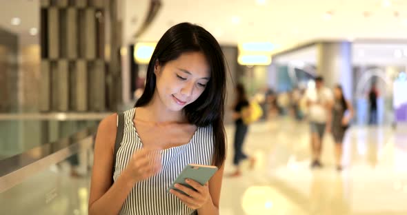 Woman looking at smart phone in shopping mall alt