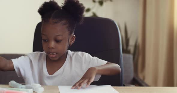 Portrait of Little Black Schoolgirl Child Sits at Home Alone Draws with Bright Colored Markers with alt