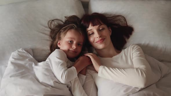 Smiling Caucasian Mommy and Daughter Relax Together at Home Lying on Bed alt