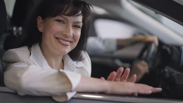 Happy Smiling Beautiful Woman Sitting on Passenger Seat in Car Looking at Camera with Blurred Man at alt