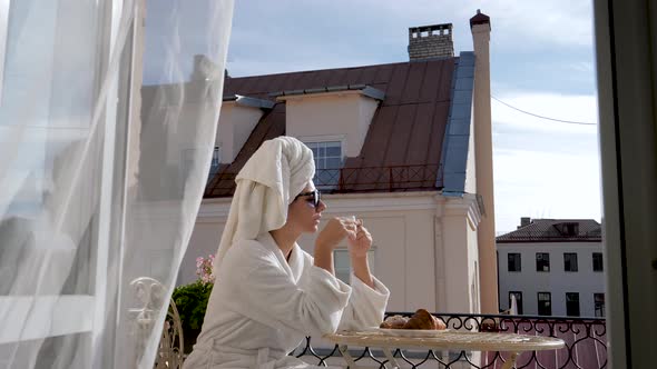 In Morning Woman In White Bathrobe Sitting On Terrace Has Breakfast With Coffee alt