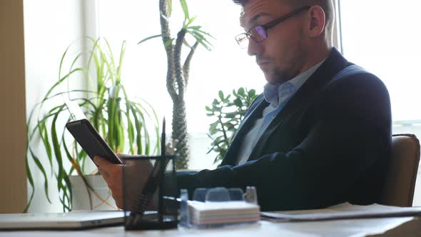 Successful Entrepreneur in Eyeglasses Analyzing Statistical Data Information on a Tablet Pc in