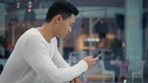 side view of Asian Male with a Phone in Big Mall or model office space alt