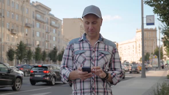Caucasian Man Stands on Street Holds Smartphone Clicks Tucks Into His Pocket alt
