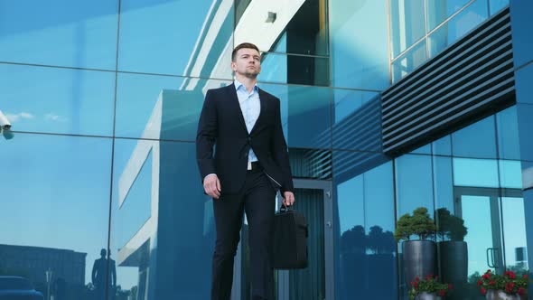 Young Businessman with a Briefcase Walking in City Street Near Modern Office Building. Confident Guy alt