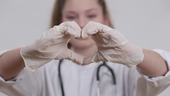Closeup Little Female Hands in Medical Gloves Showing Heart Shape with Blurred Smiling Pretty Kid alt