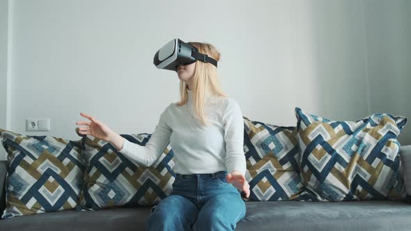 Young Blonde European Girl Lying on the Sofa Wearing Virtual Reality Headset Playing a Game alt