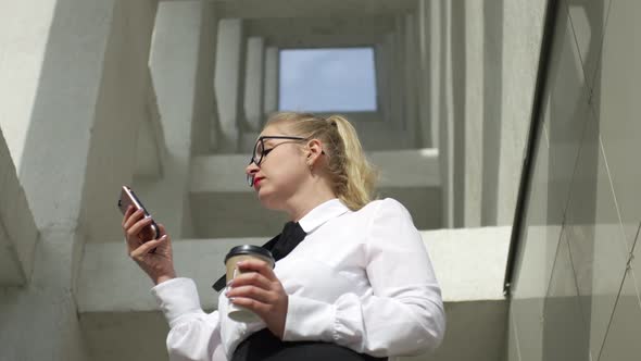 business woman with smartphone and coffee by the architectural building