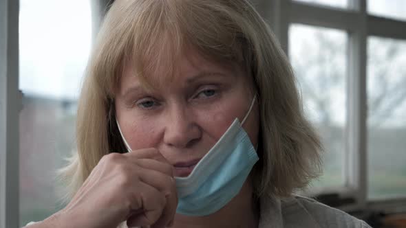 Portrait Of Mature Tired Caucasian Woman In Medical Mask On Her Face At Window alt