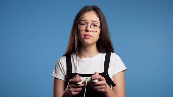 Pretty Asian Girl Playing Video Exciting Game on Tv with Joystick on Blue Studio Wall alt