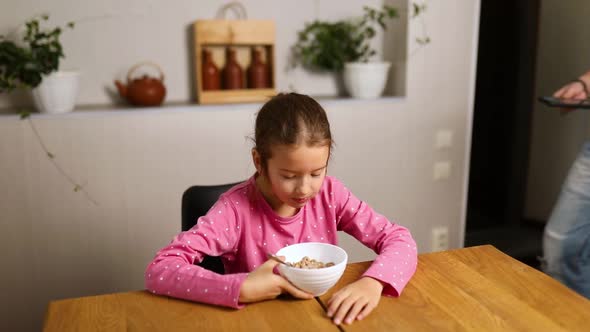 Little girl eating cereal with milk and take a phone to play game