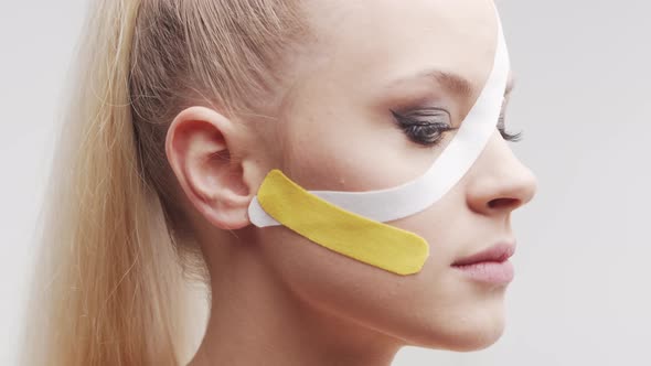 Therapist is applying kinesio tape to female face. Kinesiology and recovery treatment. alt