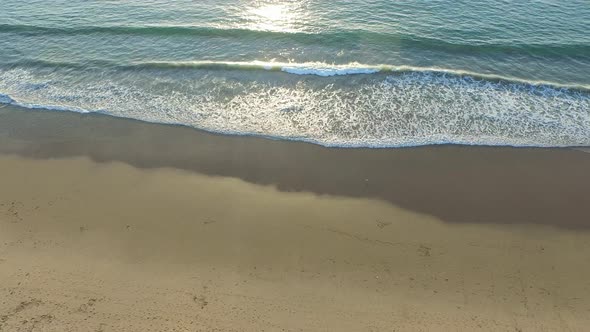 Aerial shot of the sun setting over a beach and ocean horizon. alt