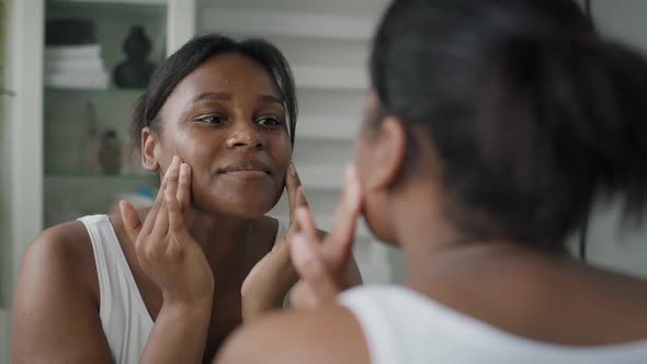 Young African-American  woman applying face cream in the mirror reflection. Shot with RED helium cam alt