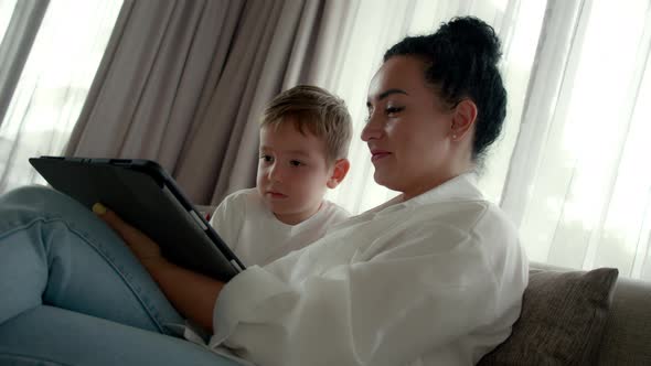 Happy Mom and Cute Son Little Child Mother Plays with Her Baby at Home Relaxing Using Smartphone alt