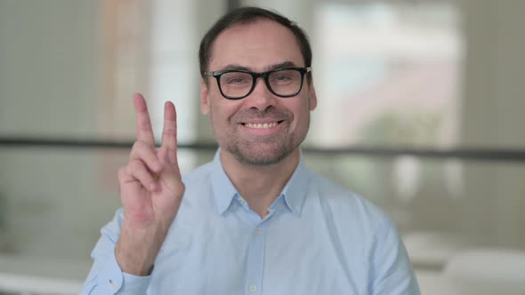 Portrait of Positive Middle Aged Man Showing Victory Sign alt