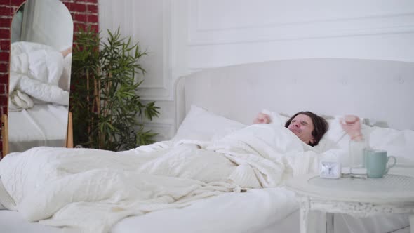 Wide Shot Portrait of Happy Rested Caucasian Brunette Man Waking Up Stretching and Leaving Bedroom alt
