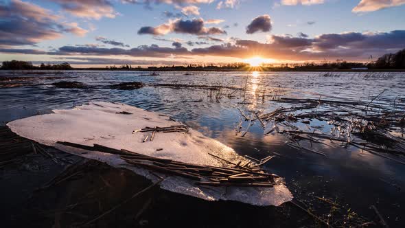 A piece of cracked ice on a shore of flooded spring river in a view of sunset sky alt