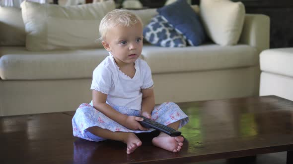 A Caucasian Toddler Girl Sitting on the Floor Watching the Tv with Remote Control alt