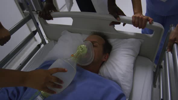 Diverse group of doctors in face masks pushing patient with oxygen mask in bed in hospital corridor alt