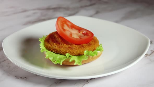 Slice of Tomato Falls on a Burger Bun With Salad and Fish Cutlet