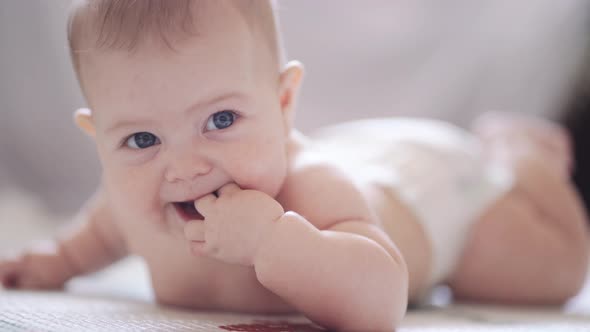 A little baby is lying on his belly against a light background and smiling alt