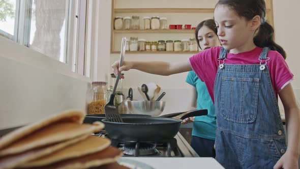 Two young girls preparing pancakes in the kitchen using a frying pan alt