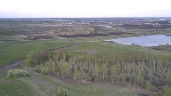 Blue Lake Among Fields Near Wide Highway Against Village alt