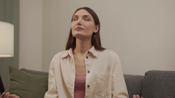 Beautiful White Girl Takes Off Her Glasses and Meditates Sitting on the Couch alt