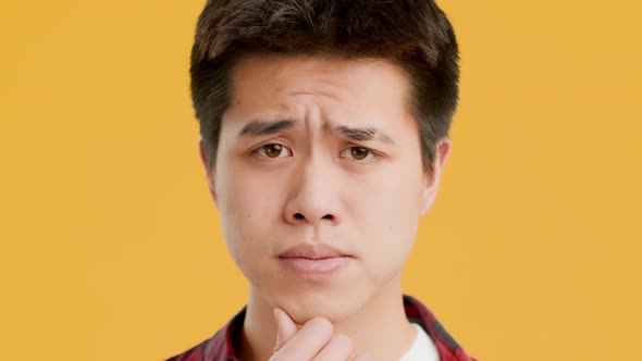 Thoughtful Asian Guy Thinking And Frowning Posing Over Yellow Background alt