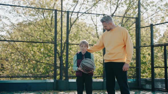 Dad Cheers His Son on at Basketball Practice on a Court on a Sunny Day