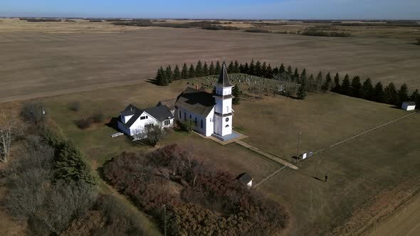 Drone orbiting around beautiful old country church in Alberta's prairies while slowly descending and alt