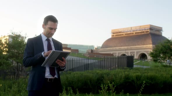 Serious Businessman Using Tablet Looks at Building in Background Turns Around and Shakes His Head in alt