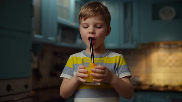 Kid holding glass of orange juice in hands, drinking it with non-plastic straw alt