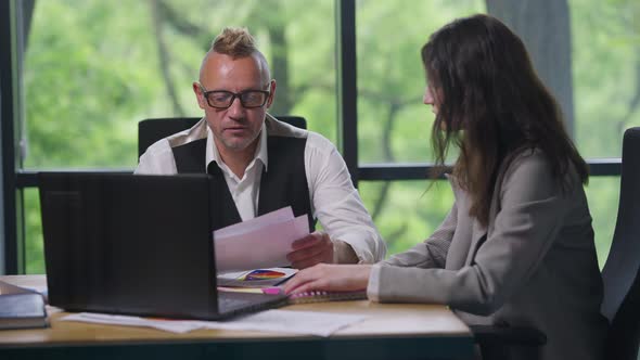 Portrait of Professional Caucasian Man Talking with Female Assistant Sitting in Office Analyzing alt