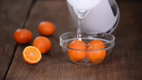 A Girl Pours Hot Water From a Teapot Into a Bowl with Tangerines