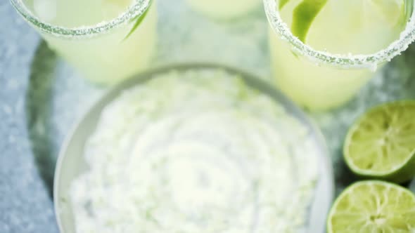 Key lime margarita garnished with fresh lime and salt in mason jar on metal tray. alt