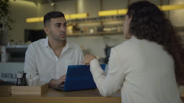Handsome Young Middle Eastern Businessman Sitting in Cafe with Caucasian Businesswoman and Using alt